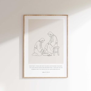 Könnte beinhalten: Ein gerahmter Wandkunstdruck mit einer schwarzen Strichzeichnung, die eine Person zeigt, die einer anderen die Füße wäscht. Unter der Illustration steht der Text: "NOW THAT I, YOUR LORD AND TEACHER, HAVE WASHED YOUR FEET, YOU ALSO SHOULD WASH ONE ANOTHER'S FEET. I HAVE SET YOU AN EXAMPLE THAT YOU SHOULD DO AS I HAVE DONE FOR YOU. John 13:14-15."