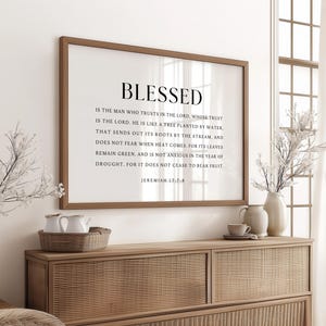 Può includere: Una stampa incorniciata con la parola "BLESSED" e un versetto biblico. La stampa è in una cornice marrone e appesa sopra un mobile in legno. Il mobile ha una trama intrecciata sul davanti. Vasi decorativi e un vassoio con tazze da tè sono sul mobile.