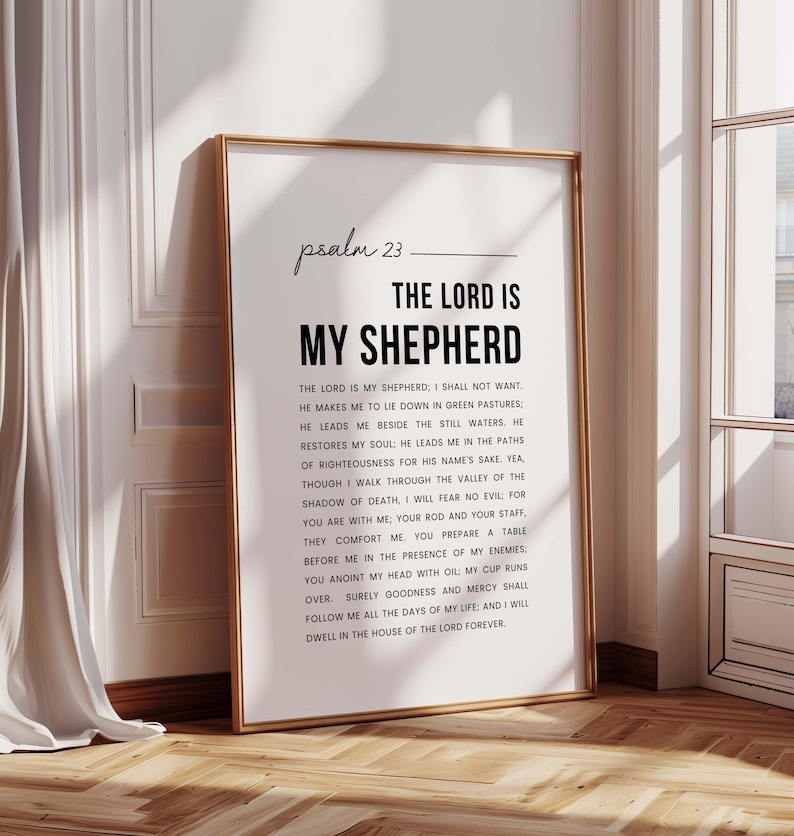May include: A framed print with the text of Psalm 23, featuring the words "The Lord is My Shepherd" in bold. The print is in a gold frame and leans against a white wall and wooden floor, creating a warm, inviting aesthetic.