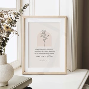May include: A framed print in a light wood frame. The print displays a floral line drawing and the text "For I know the plans I have for you...hope and a future" from Jeremiah 29:11. The background is a soft beige colour.