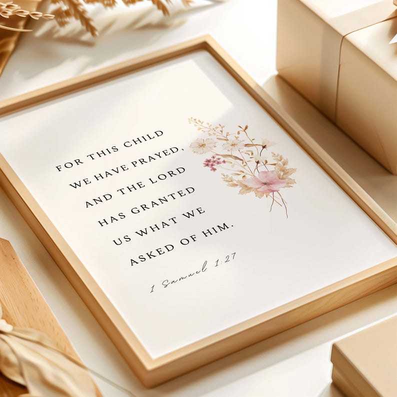 May include: A framed print with the text "FOR THIS CHILD WE HAVE PRAYED, AND THE LORD HAS GRANTED US WHAT WE ASKED OF HIM. 1 Samuel 1.27." The print has a light wood frame and a floral design in the upper right corner. The flowers are in shades of pink, beige, and white.