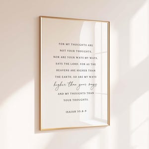 May include: A framed print with a gold border displays a religious quote from Isaiah 55:8-9. The text is in black, with the words "higher than your ways" in a cursive font. The background is a light beige.