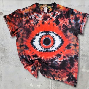Könnte beinhalten: Ein Batik-T-Shirt mit einem großen roten, weißen und schwarzen Augenmotiv. Das Shirt ist dunkelrot mit schwarzen und weißen Wirbeln.