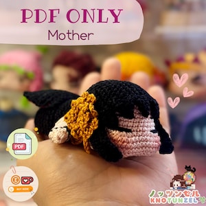 Puede incluir: Patrón PDF para tejer una muñeca amigurumi dormida con cabello negro, una flor amarilla y mejillas rosadas. La muñeca está acostada en una mano. El texto "PDF ONLY Mother" está en la parte superior de la imagen.