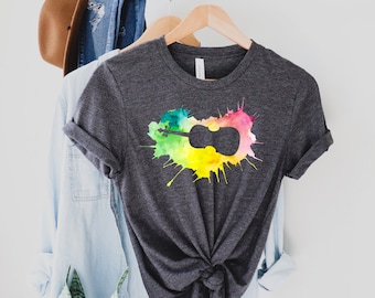 May include: A dark grey t-shirt with a colourful watercolour design of a violin. The design features shades of green, yellow, pink, and blue.