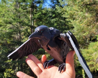 Puede incluir: Una figura de cuervo negro articulada con plumas moldeadas detalladas, un pico afilado y alas extendidas. El ave está construida con material plástico oscuro con articulaciones visibles en los hombros, lo que permite ajustar la posición de las alas.
