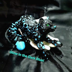 May include: A black and blue jaguar figurine with green eyes. The jaguar has blue spots and is posed in a crouching position. The text "Glow in the Dark Blue!" is visible.