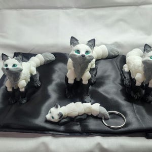 May include: Three white and gray fox figurines with green eyes. The foxes are posed in a sitting position with their tails curled around their bodies. One fox is attached to a silver key chain.