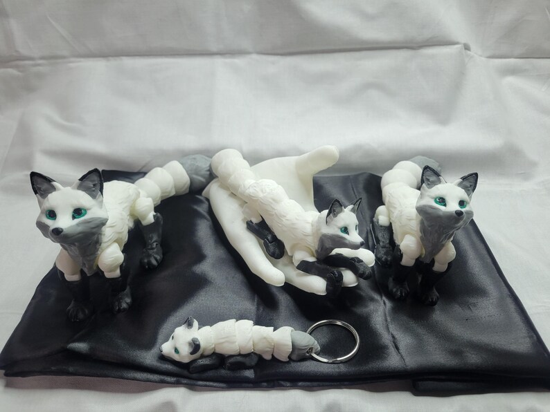 May include: Four white and gray fox figurines with black eyes. The foxes are posed in different positions, including sitting, lying down, and standing. The figurines are made of a smooth, white material and have a realistic appearance.