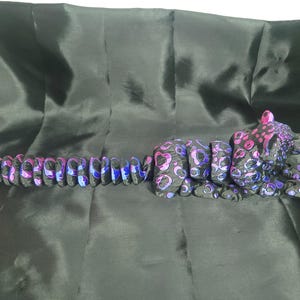 May include: A black and purple leopard sculpture with a segmented body and a spotted pattern. The leopard's body is made up of connected pieces, and the spots are in shades of pink and purple. The sculpture is lying on a black surface.