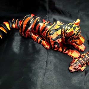 Könnte beinhalten: Handgefertigte Tigerfigur mit Jungtier, mit orangefarbenen und schwarzen Streifen. Der Tiger liegt, und das Jungtier befindet sich in der Nähe. Die Figuren sind vor einem dunklen Hintergrund platziert, der die lebendigen Farben und die detaillierte Handwerkskunst hervorhebt.
