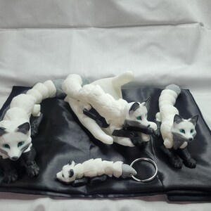 May include: Four white and black fox figurines with green eyes. The foxes are in different poses, including curled up, sitting, and standing. The figurines are on a black fabric background.