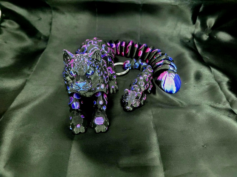 May include: A black and purple jaguar figurine with a matching tail and a smaller cub. The jaguar has blue accents and a silver key ring. The tail is a series of connected beads in shades of purple, pink, and blue.