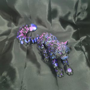 May include: A black and purple leopard figurine with a spotted pattern. The sculpture has a long tail and is posed in a stalking position. The leopard's spots are a mix of purple and blue.