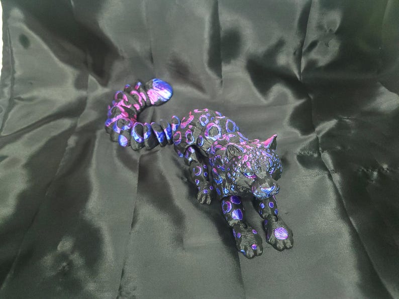 May include: A black and purple leopard figurine with a spotted pattern. The sculpture has a long tail and is posed in a stalking position. The leopard's spots are a mix of purple and blue.