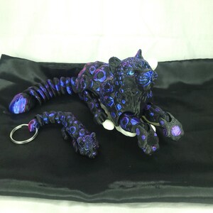 May include: A black and purple jaguar figurine and keychain set. The jaguar has a spotted pattern with blue and purple accents. The keychain features a smaller jaguar with a silver ring.