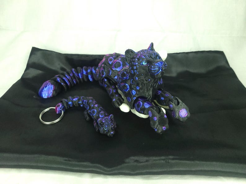 May include: A black and purple jaguar figurine and keychain set. The jaguar has a spotted pattern with blue and purple accents. The keychain features a smaller jaguar with a silver ring.