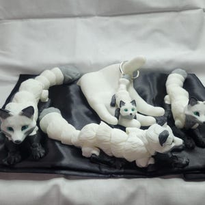 May include: Four white and gray ceramic fox figurines with green eyes. The foxes are arranged on a black satin fabric. One fox is holding a key chain.