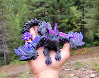 May include: A black articulated dragon figurine with vibrant purple accents on its wings, ears, and tail. The creature features detailed scales, sharp claws, and bright blue eyes, designed with a multi-jointed body structure for movement.