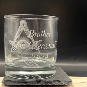 May include: Clear glass tumbler with etched Masonic symbols and the words "Brother Jon Zerwinski 2024". The glass sits on a dark gray square coaster, with a black background.