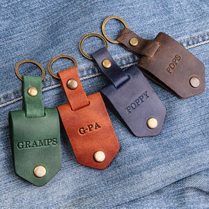 May include: Five leather keychains with metal rings and engraved names. The keychains are green, brown, blue, and orange. The names on the keychains are "Gramps", "G-PA", "Poppy", "Pops".
