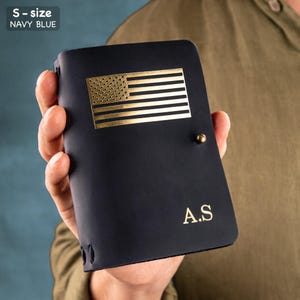 May include: Navy blue leather wallet with a gold-colored American flag emblem. The wallet has the initials "A.S" in gold lettering. The text "S - size NAVY BLUE" is in the upper left corner.