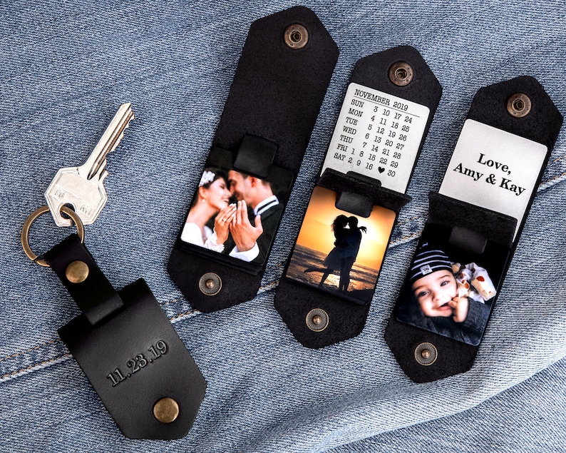 May include: Four black leather keychains with different photo inserts. The first keychain has a photo of a couple getting married. The second keychain has a photo of a couple kissing at sunset. The third keychain has a photo of a baby boy. The fourth keychain has a calendar for November 2019. The text "Love, Amy & Kay" is engraved on the fourth keychain.