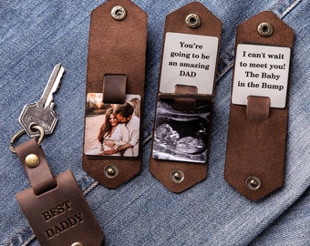 May include: A brown leather keychain with a photo insert and a message that says "You're going to be an amazing DAD". The keychain also has a separate tag that says "BEST DADDY".