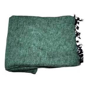 Op de afbeelding: Een opgevouwen groene deken met een geweven textuur. De deken heeft een donkere franje aan &eacute;&eacute;n rand. De deken is gemaakt van een zacht materiaal en is geschikt voor gebruik als sprei of omslag.