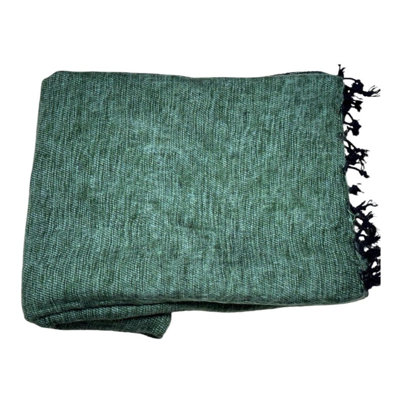 Op de afbeelding: Een opgevouwen groene deken met een geweven textuur. De deken heeft een donkere franje aan &eacute;&eacute;n rand. De deken is gemaakt van een zacht materiaal en is geschikt voor gebruik als sprei of omslag.