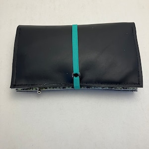 Könnte beinhalten: Eine schwarze Ledergeldbörse mit einem türkisfarbenen Gummibandverschluss.