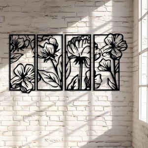 May include: Four-panel black metal floral wall art. Each panel features a different flower design with stems and leaves. The artwork is mounted on a white brick wall, with sunlight streaming in from a window.