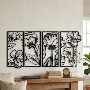 May include: Four-panel black metal floral wall art. Each panel features a different stylized flower design. The art is mounted on a white wall above a wooden table with books, a clock, and decorative items.