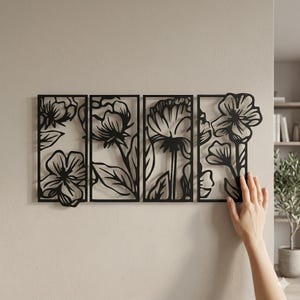 May include: Black metal floral wall art composed of four rectangular panels. Each panel features a different flower design with leaves and stems. The art is mounted on a light beige wall, creating a contrast with the dark metal.