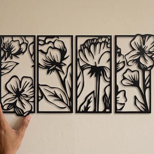 May include: Four black metal floral wall art panels. Each panel features a different flower design with intricate cut-out details. The panels are rectangular and arranged side by side, creating a cohesive decorative piece for any room.