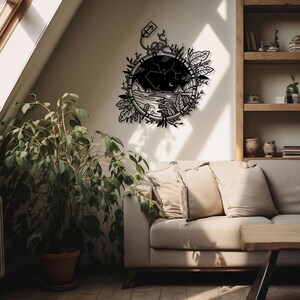 Puede incluir: Arte de pared de metal negro con un dise&ntilde;o circular que contiene una constelaci&oacute;n. La constelaci&oacute;n est&aacute; rodeada de hojas y enredaderas. El arte est&aacute; colgado en una pared blanca sobre un sof&aacute; beige con almohadas.