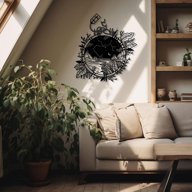 Puede incluir: Arte de pared de metal negro con un dise&ntilde;o circular que contiene una constelaci&oacute;n. La constelaci&oacute;n est&aacute; rodeada de hojas y enredaderas. El arte est&aacute; colgado en una pared blanca sobre un sof&aacute; beige con almohadas.