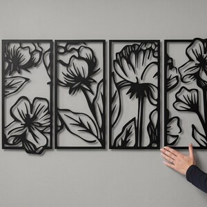 May include: Four black metal floral wall art panels. Each panel features a different flower design with leaves, creating a cohesive botanical theme. The panels are rectangular and mounted on a gray wall.