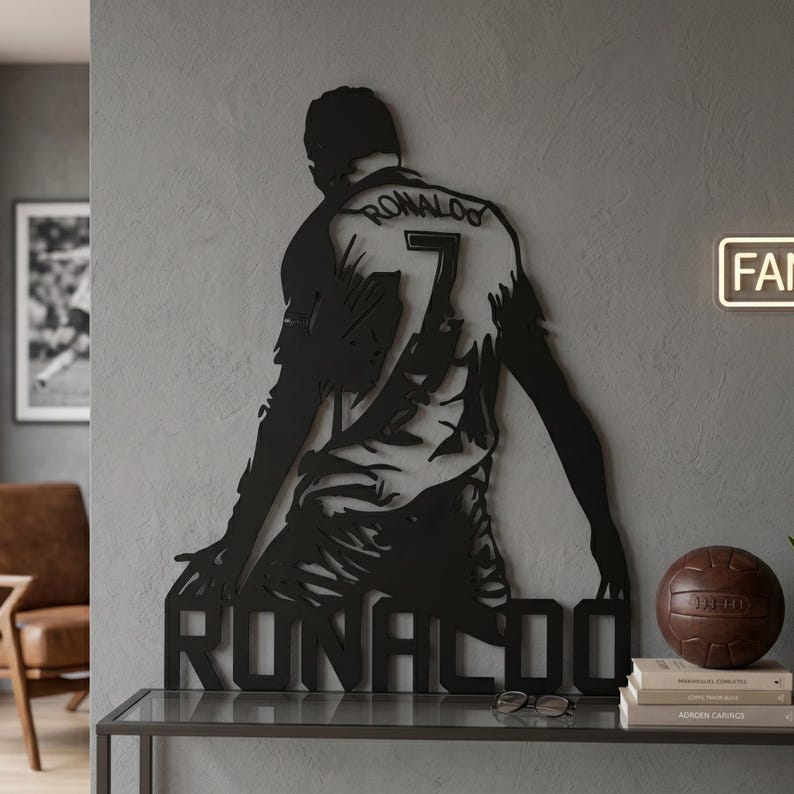 Op de afbeelding: Zwarte metalen wandkunst met een voetballer in knielende houding, met de naam "RONALDO" onderaan en het nummer "7" op het shirt. De naam van de speler staat ook op de achterkant van het shirt. Een decoratief stuk voor sportfans.