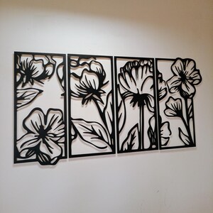 May include: A four-panel wall art piece featuring a floral design. Each panel is a black silhouette of flowers and leaves against a white background. The artwork is a modern, decorative accent for any room.