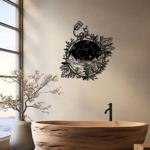 Puede incluir: Arte de pared de metal negro con un dise&ntilde;o circular que representa una escena de cielo nocturno, una luna creciente y una constelaci&oacute;n de estrellas. El dise&ntilde;o incluye una cordillera, una masa de agua y un borde floral. La constelaci&oacute;n est&aacute; etiquetada como "Sagitario".