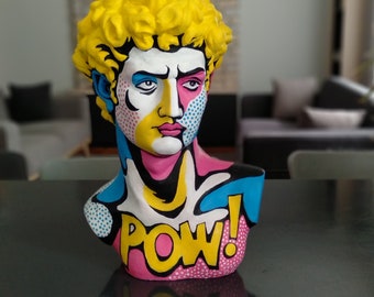 May include: A yellow, blue, pink, and black pop art bust sculpture of a person with the word "POW!" on the chest.