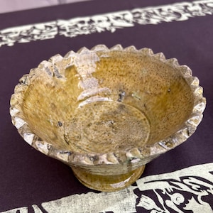 May include: A small, brown ceramic bowl with a scalloped rim and a textured glaze. The bowl has a slightly raised base.