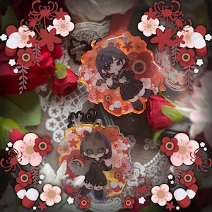May include: Two circular acrylic charms featuring anime-style characters in black school uniforms. The top charm shows a character with short dark hair, while the bottom charm depicts a character wearing a fox mask. Both have orange floral backgrounds.