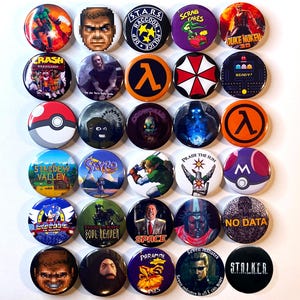 Könnte beinhalten: Eine Sammlung von dreißig runden Ansteckbuttons mit verschiedenen Videospielcharakteren, Logos und Textgrafiken, darunter Stardew Valley, Sonic, Duke Nukem, Crash Bandicoot, S.T.A.R.S., Lambda, Umbrella Corporation und No Data.
