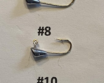 Może przedstawiać: Trzy główki jigowe do wędkowania o wadze 1/64 uncji. Główki jigowe są srebrne z złotymi haczykami. Rozmiary to #6, #8 i #10.