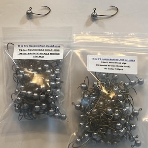May include: Two bags of 1/24oz roundhead jig fishing lures with #6 Mustad bronze sickle hooks. The bags contain 100 pieces each. One bag has a label that says "EC Bronze Sickle Hooks" and the other says "No Collar 100pcs".