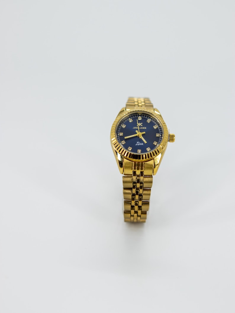 May include: A gold-tone wristwatch with a blue face and a gold metal band. The watch face has a white dial with black hour and minute hands, and a small second hand. The watch face also has a small date window at the 3 o'clock position. The watch band is a traditional link style.
