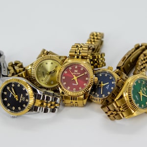 May include: A group of five gold-tone wristwatches with different colored faces. The watches have a variety of band styles, including gold, silver, and two-tone.