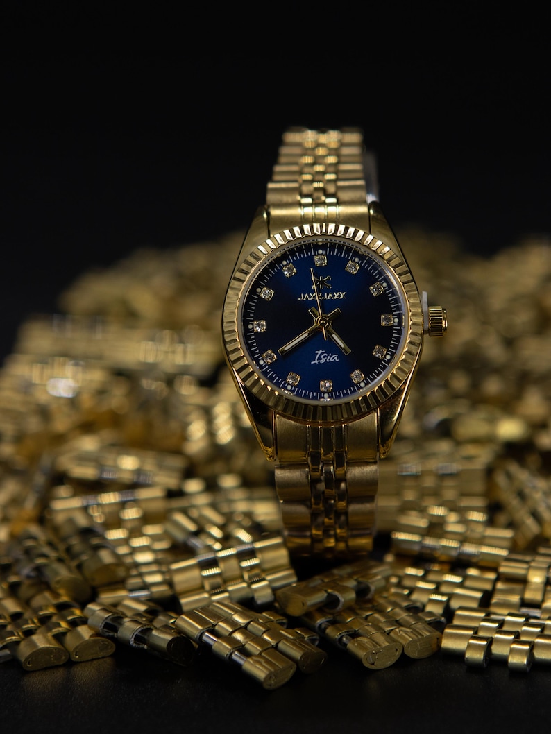 May include: A gold-tone wristwatch with a blue face and a gold metal band. The watch face has a gold-tone border with small diamonds around the edge. The watch face also has a gold-tone logo and the word "Isia" printed on it.